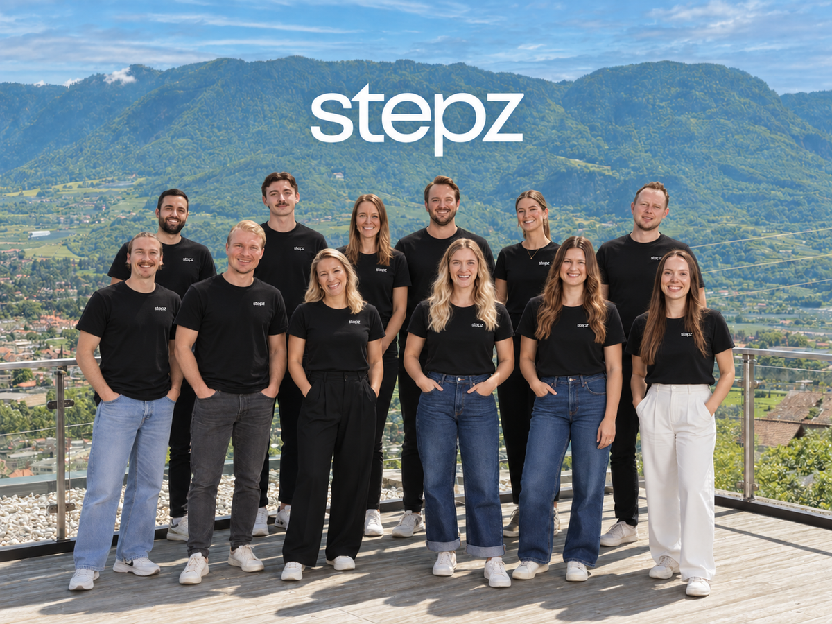 Das stepz Team in schwarzen stepz T-Shirts auf einer Terrasse mit Bergblick.